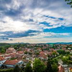 A scenic aerial view of a picturesque village with red-roofed houses under a dramatic sky.