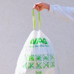 Hand holding an eco-friendly recyclable plastic bag with green symbols and labels against a white background.