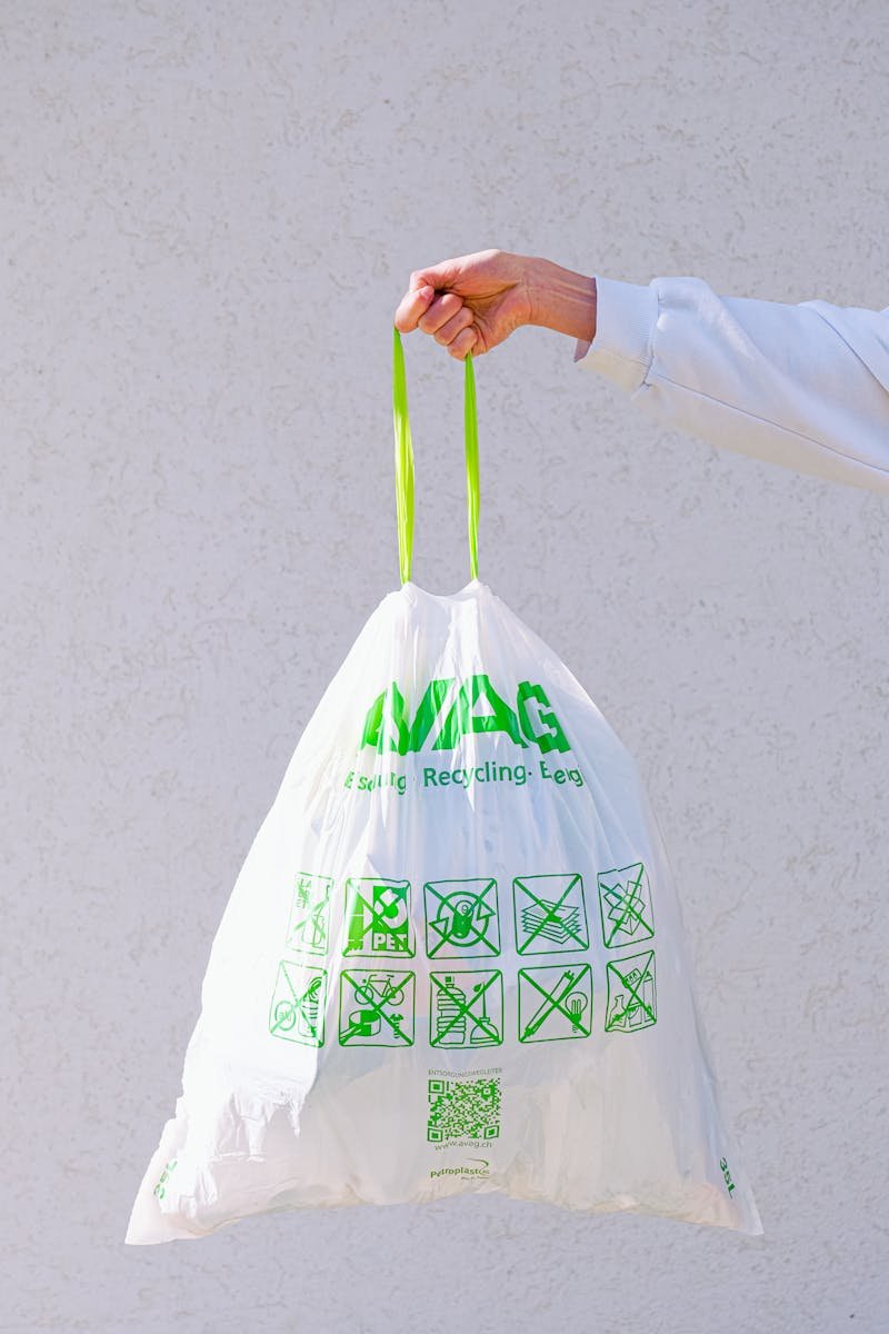 Hand holding an eco-friendly recyclable plastic bag with green symbols and labels against a white background.