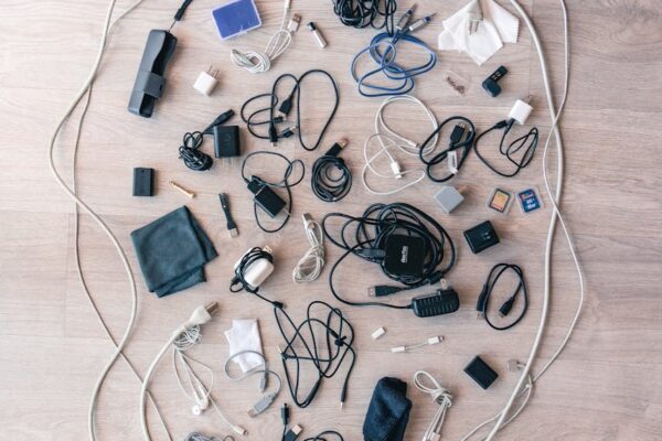 A variety of electronic cables, chargers, and accessories arranged in a flat lay on a wooden floor.