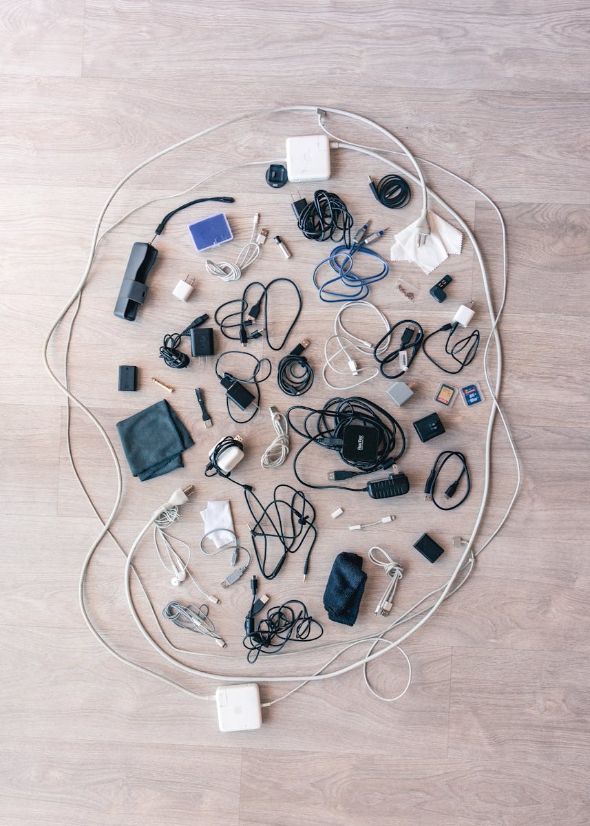 A variety of electronic cables, chargers, and accessories arranged in a flat lay on a wooden floor.