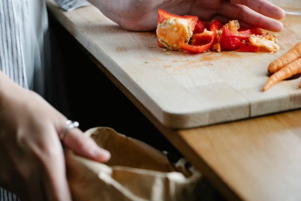 Crop anonymous housewife throwing vegetable leftovers on chopping board while cooking in light kitchen