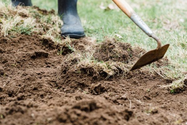 Crop unrecognizable farmer in dirty rubber boots standing and loosening dry soil in countryside in daylight