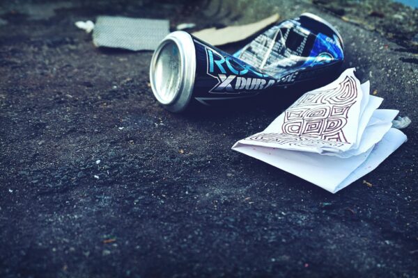 A crumpled beverage can and papers litter an urban street, highlighting environmental issues.
