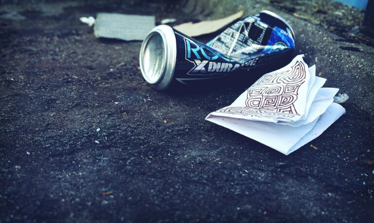 A crumpled beverage can and papers litter an urban street, highlighting environmental issues.