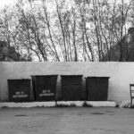 Monochrome photo of urban garbage bins and a solitary chair in a residential area.