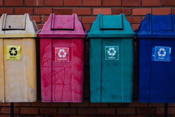 Four colorful recycling bins for metal, plastic, glass, and paper against a brick wall in Brazil.