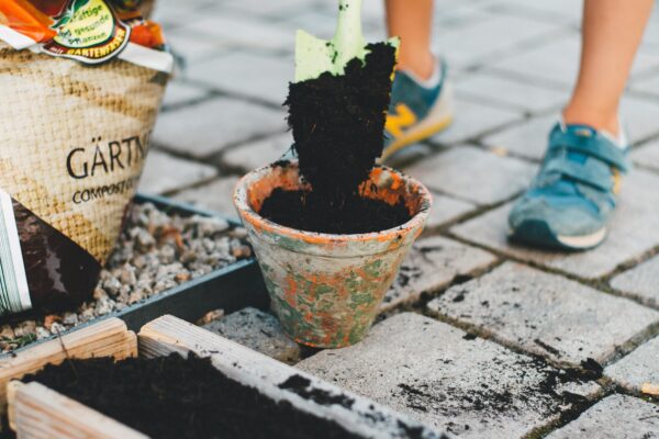 A child actively participates in gardening by shoveling soil into a pot on a patio.