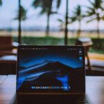 A sleek laptop on a wooden desk with a tropical view behind, ideal for remote work and travel themes.