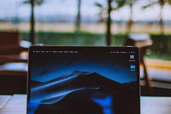 A sleek laptop on a wooden desk with a tropical view behind, ideal for remote work and travel themes.