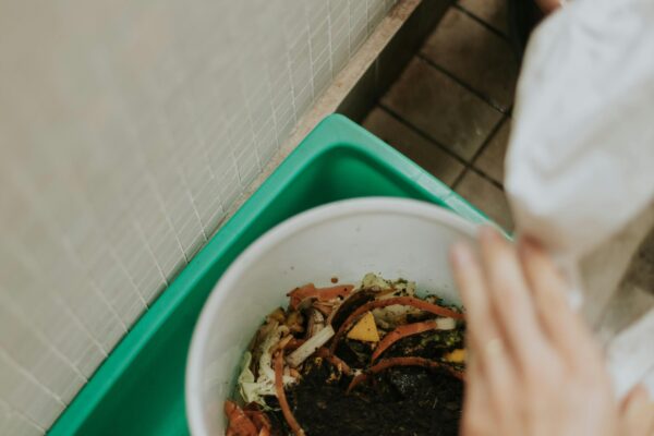 View of hands adding food scraps to a compost bin with visible soil.