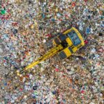 Aerial shot of a landfill with a yellow excavator in South Tangerang, Indonesia.