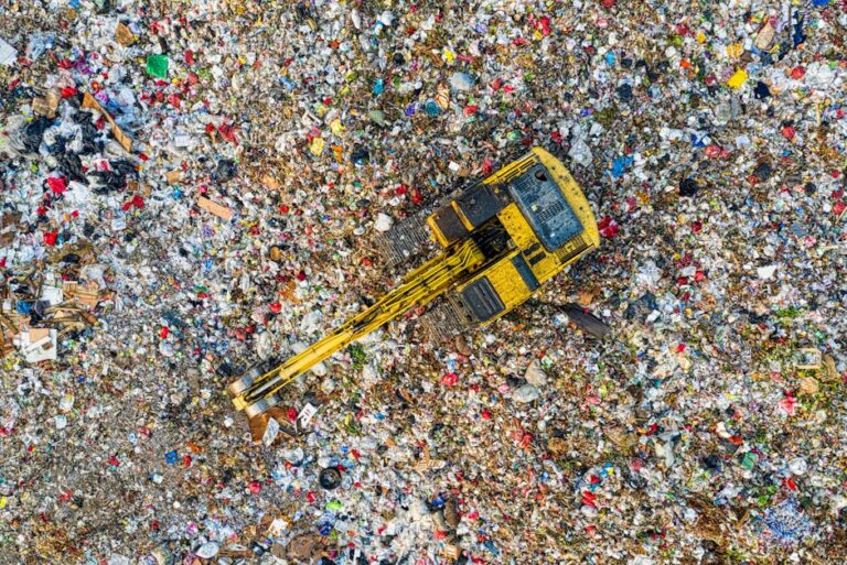 Aerial shot of a landfill with a yellow excavator in South Tangerang, Indonesia.