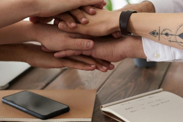 Hands from a diverse team stack on a table symbolizing unity and teamwork in a modern office setting.