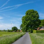 Scenic summer landscape featuring a rural road, wind turbine, and vibrant greenery under a blue sky.