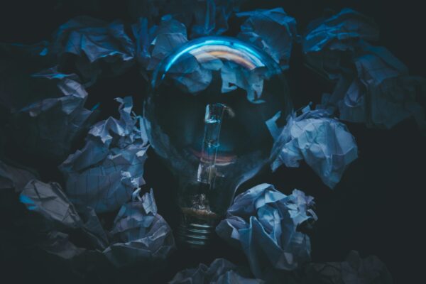 A light bulb surrounded by crumpled paper symbolizes creative ideas and innovation in a dark setting.