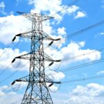 Electricity pylon with high voltage lines set against a vibrant blue sky with clouds.