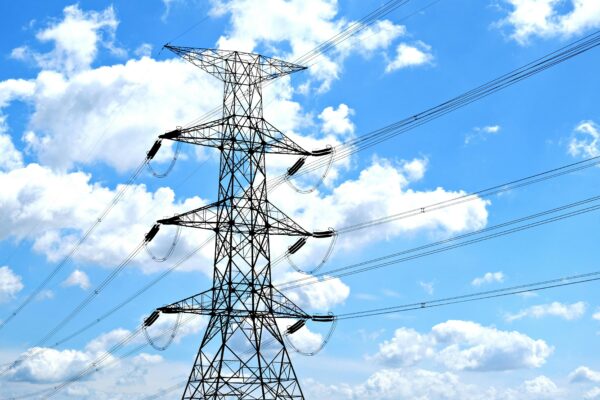 Electricity pylon with high voltage lines set against a vibrant blue sky with clouds.