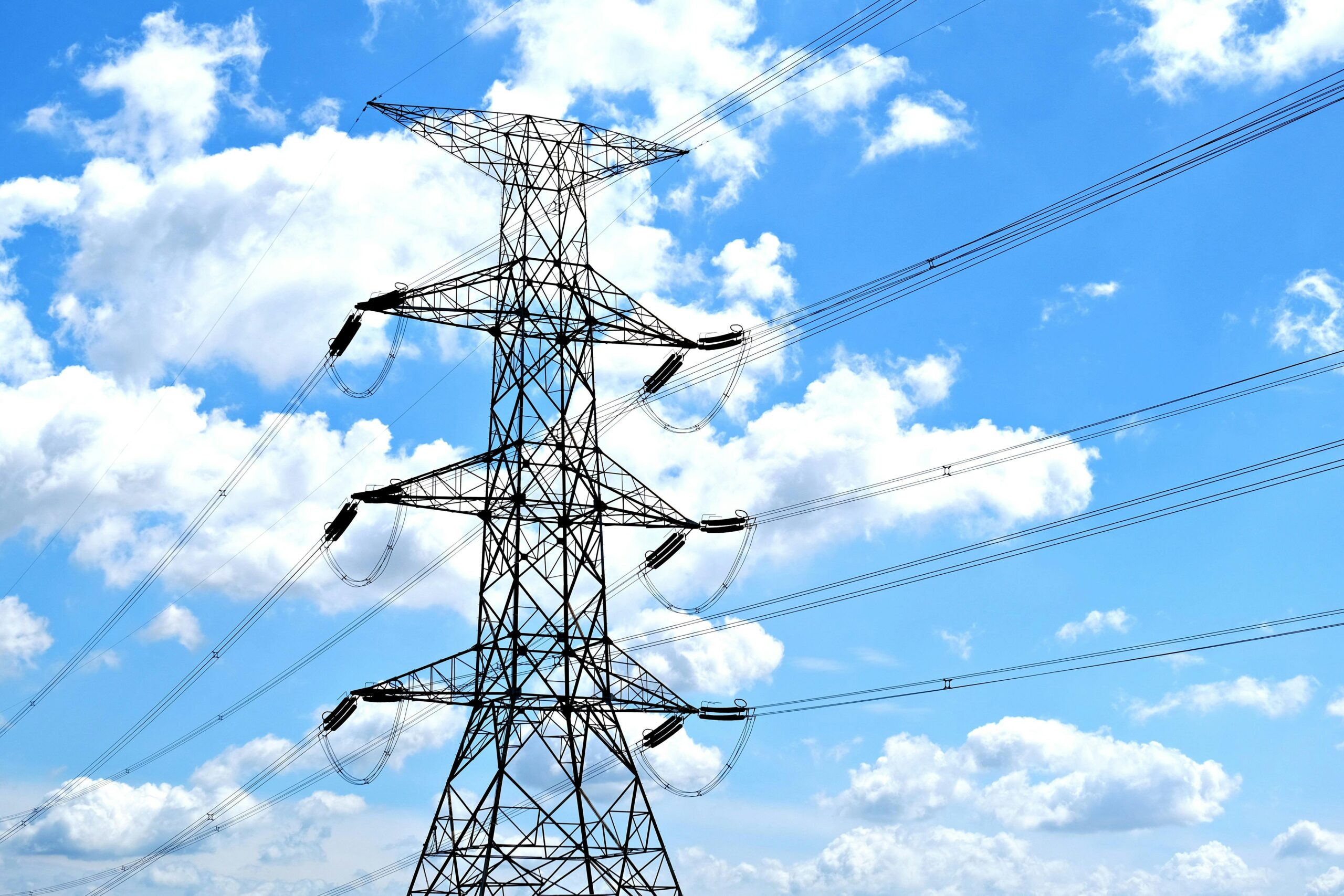 Electricity pylon with high voltage lines set against a vibrant blue sky with clouds.