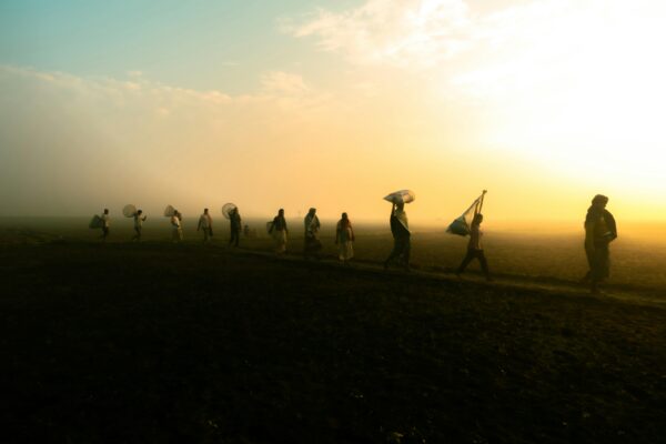A group of silhouetted villagers walking at sunrise on a misty morning in rural Bangladesh.