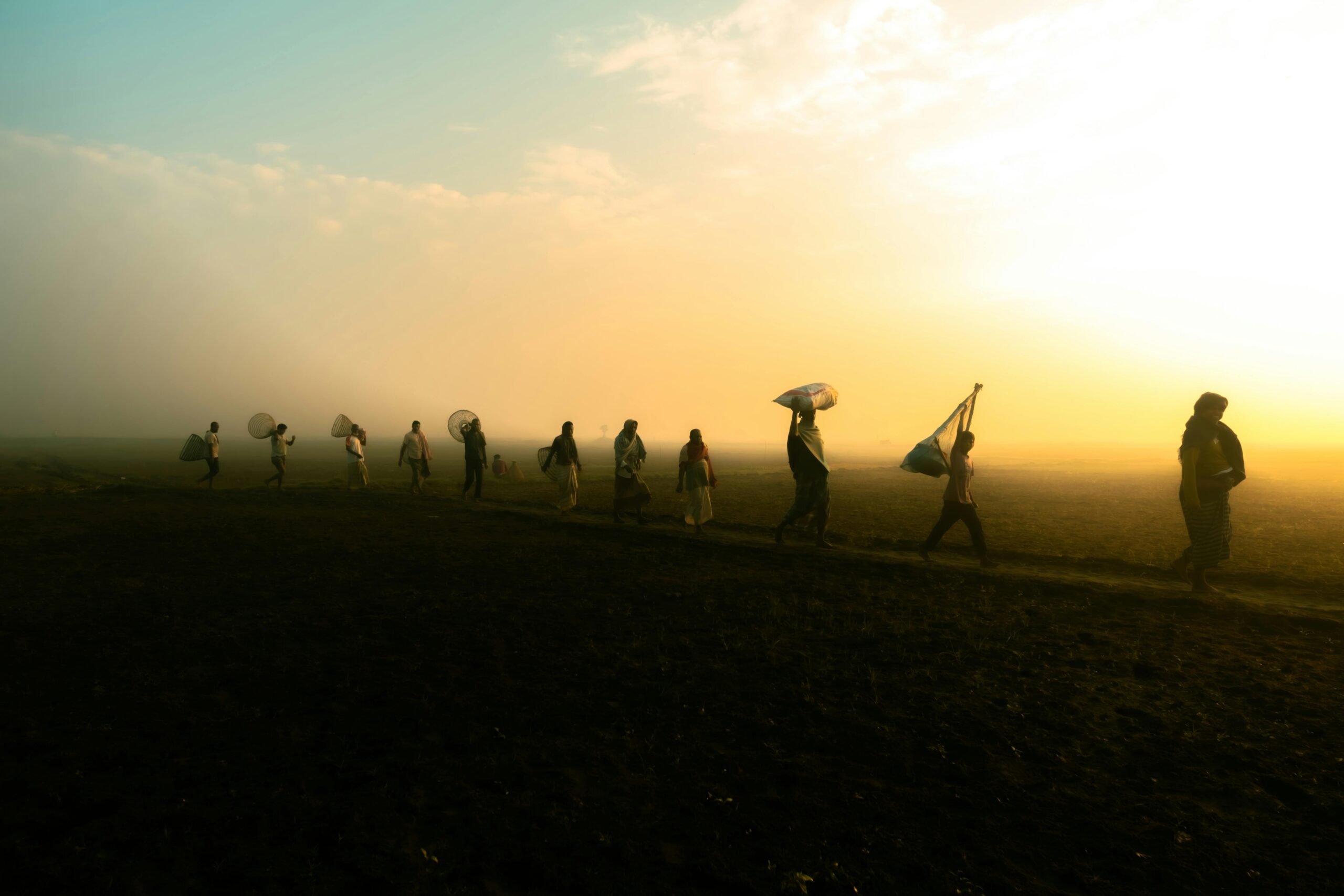 A group of silhouetted villagers walking at sunrise on a misty morning in rural Bangladesh.