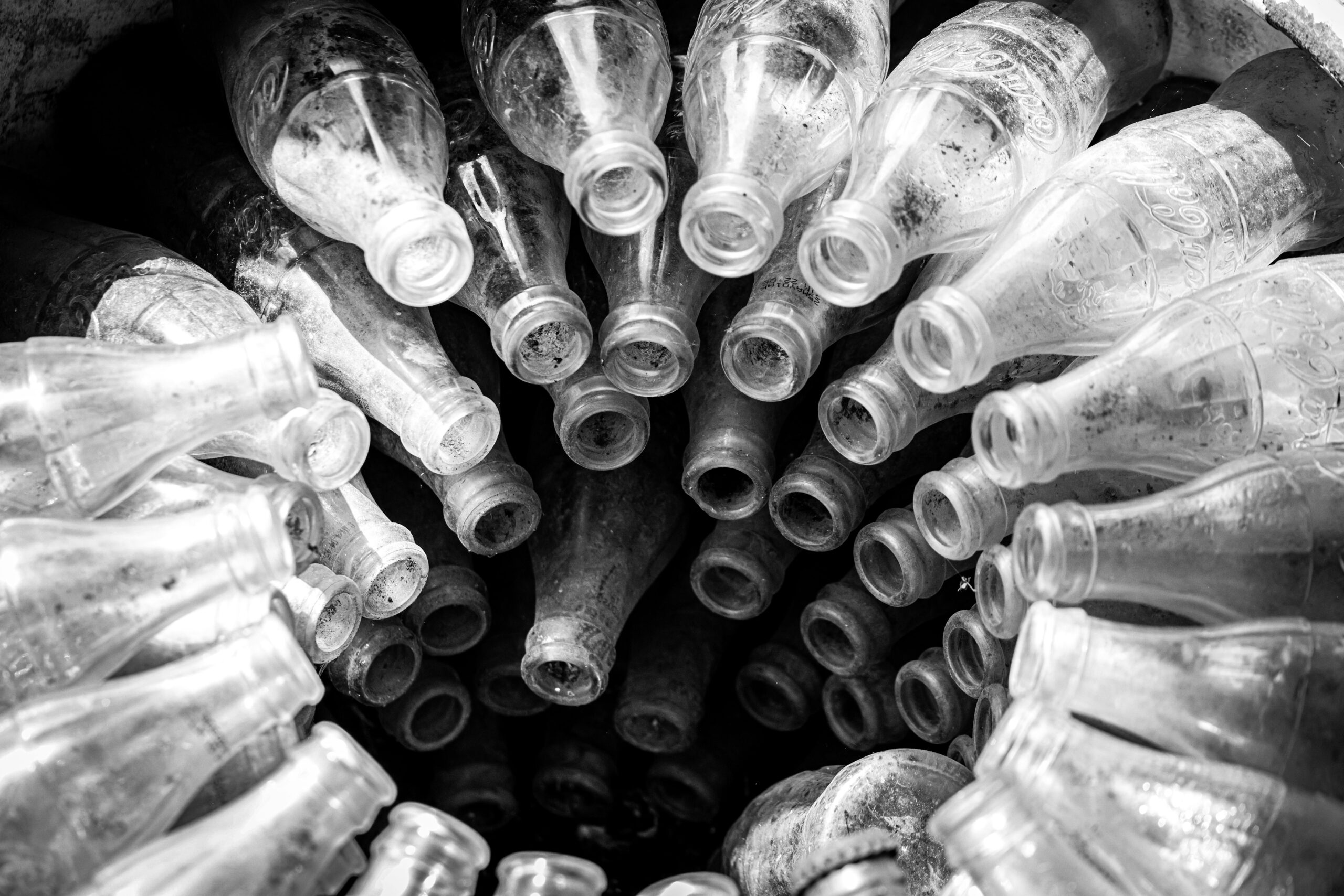 Black and white photo showcasing a spiral arrangement of empty vintage glass bottles.