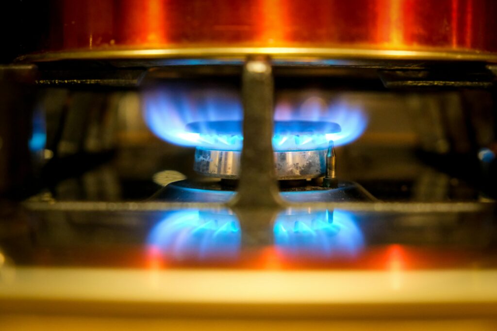 Gambar saat ini: Close-up of a blue flame on a gas stove burner, showcasing kitchen heat and cooking.