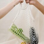 Hands holding a mesh bag filled with fresh vegetables, promoting sustainable shopping practices.