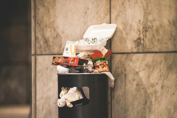A trash can overflowing with garbage in an urban setting, against a concrete wall.