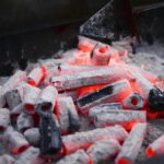 Small hexagonal coals with holes smoldering on metal rack before roasting barbecue in nature