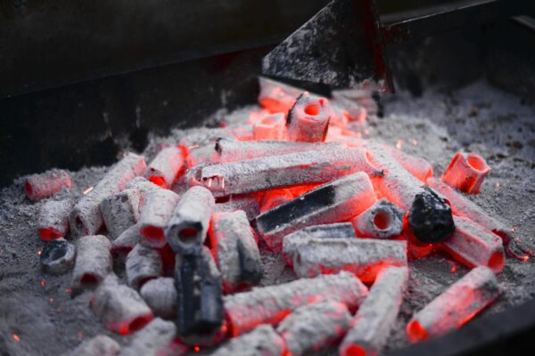 Small hexagonal coals with holes smoldering on metal rack before roasting barbecue in nature