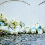 Yellow garbage bags piled against a white wall on a cobblestone street corner outdoors.