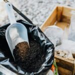 Close-up of gardening essentials with soil scoop, bag, and wooden box in garden setting.