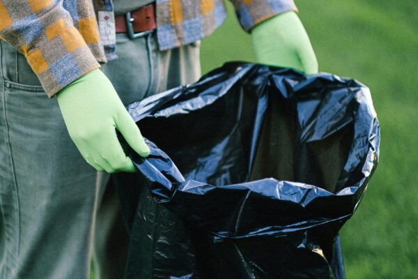 Person wearing gloves holding a trash bag in a green field, emphasizing volunteer cleanup efforts.