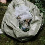 Bag filled with litter on mossy forest floor, highlighting environmental awareness.