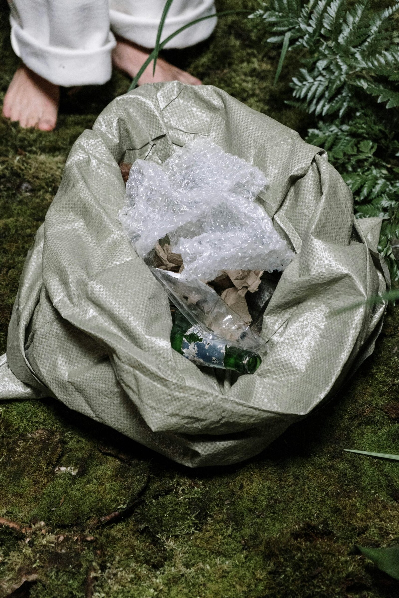 Bag filled with litter on mossy forest floor, highlighting environmental awareness.