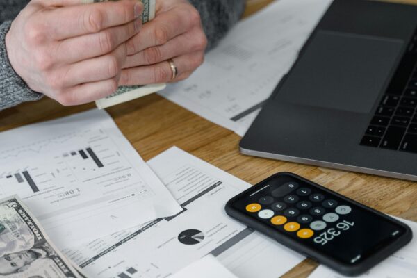 Hands counting money at a workspace with a laptop, calculator, and financial documents.