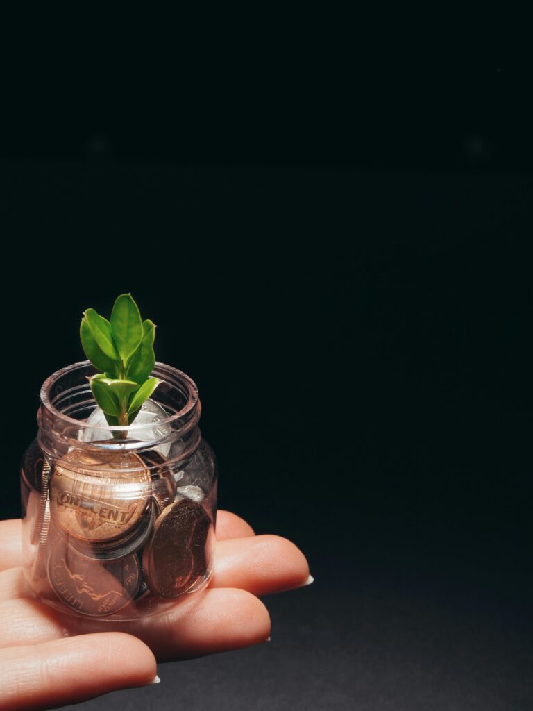 A small plant growing in a glass jar filled with coins, represents financial growth and sustainability.
