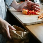 Crop anonymous housewife throwing vegetable leftovers on chopping board while cooking in light kitchen