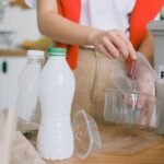 An adult woman sorts plastic containers into a recycling bin in a kitchen.