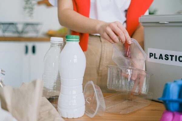 An adult woman sorts plastic containers into a recycling bin in a kitchen.