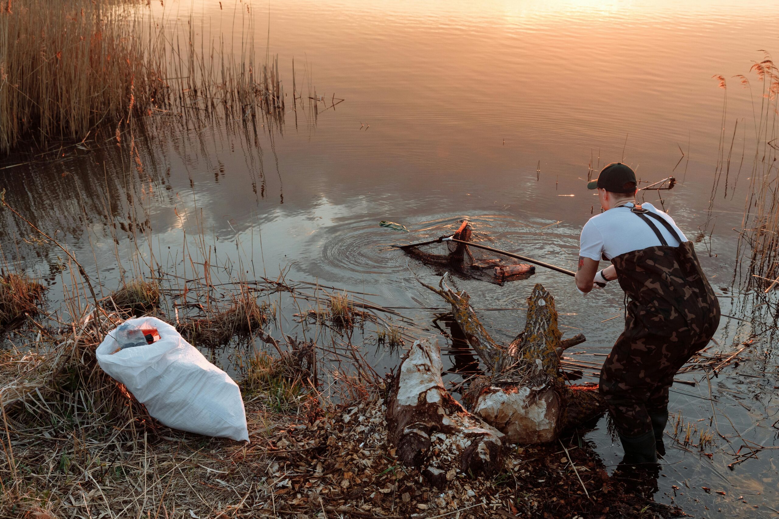 Man cleaning lake banks using a net, promoting environmental conservation.