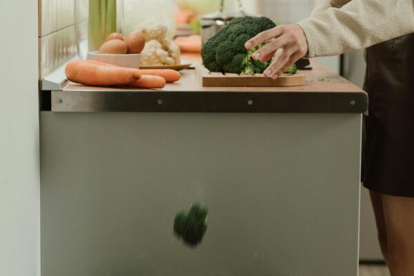 Person discarding broccoli in a stylish kitchen with fresh vegetables on the counter.