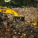 Excavator and worker managing waste at a landfill site, highlighting pollution issues.