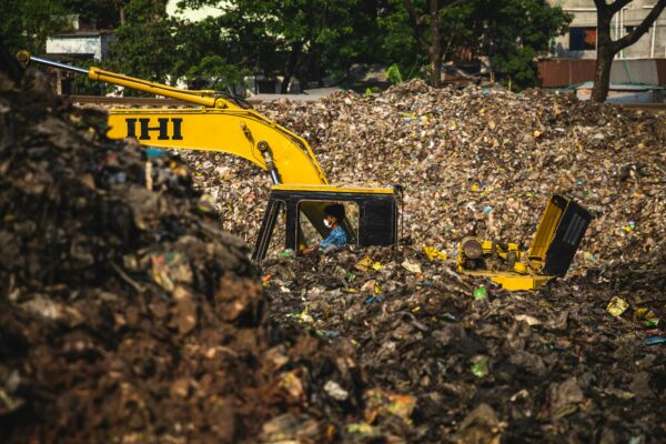 Excavator and worker managing waste at a landfill site, highlighting pollution issues.