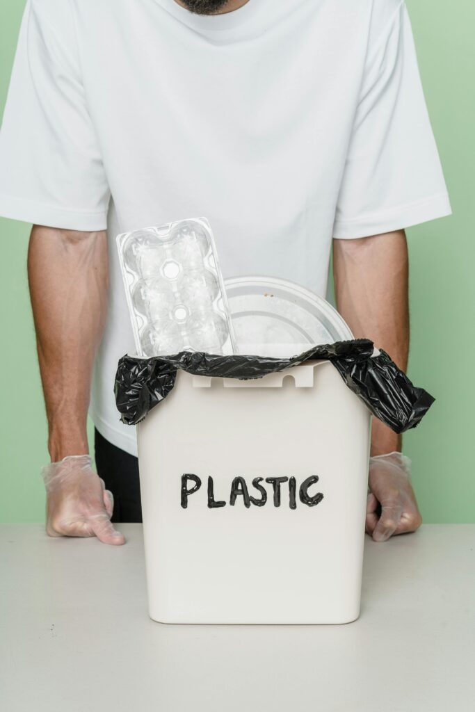 Adult male with gloves standing by a plastic recycling bin full of waste.
