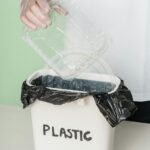 A person disposing of a plastic tray into a recycling bin, promoting eco-friendly habits.