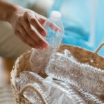 Close-up of a person sorting plastic bottles into a basket for recycling indoors.
