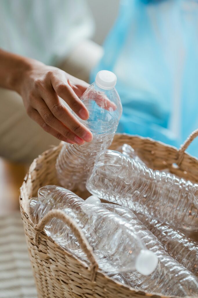 Close-up of a person sorting plastic bottles into a basket for recycling indoors.