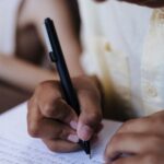 Child's hands writing with a pen on paper indoors, showing focus and concentration.
